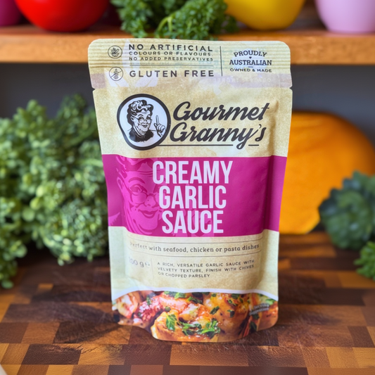 Packaging of Gourmet Granny's Creamy Garlic Sauce on a wooden surface with vegetables in the background.