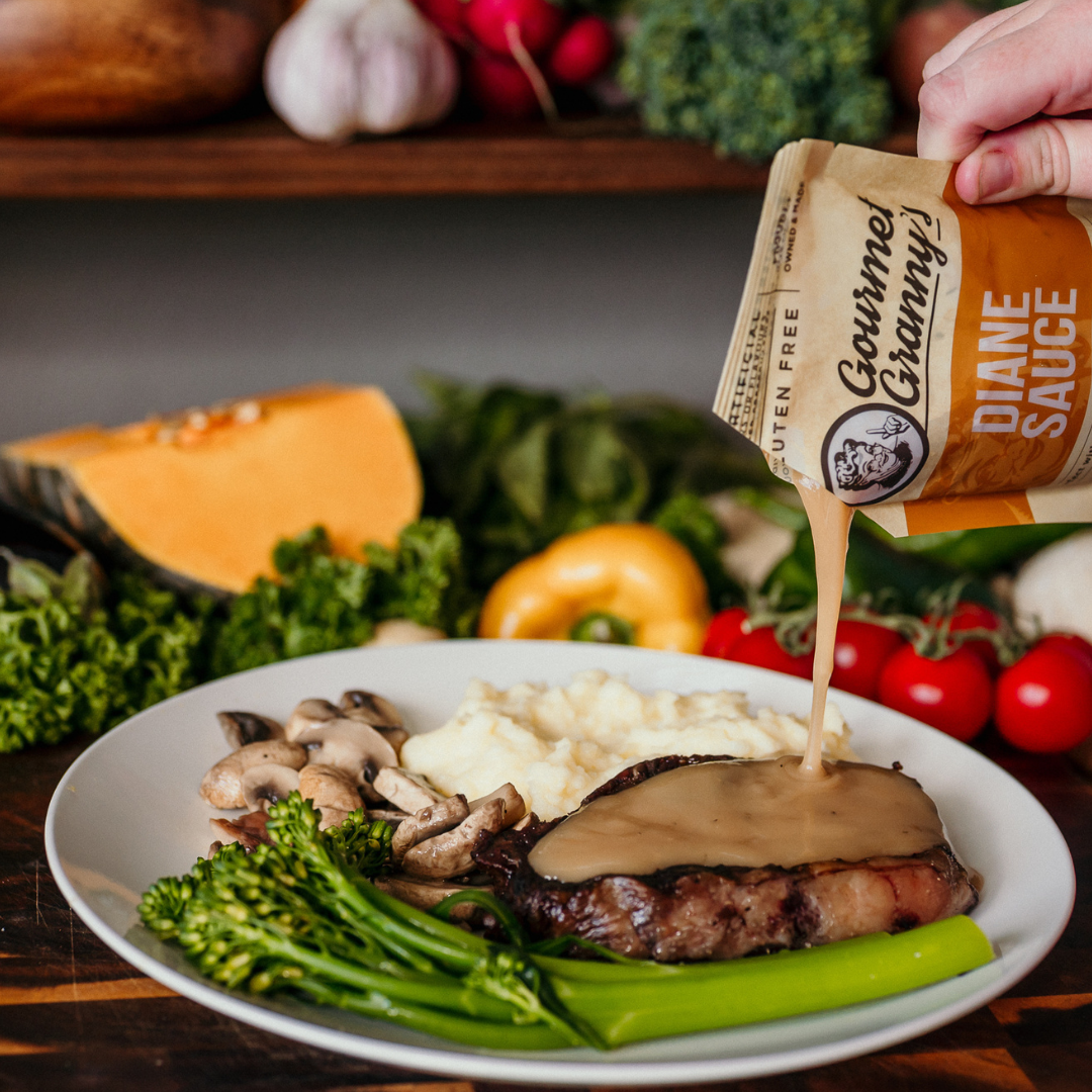 Person pouring Diane sauce over a plate of food with vegetables in the background