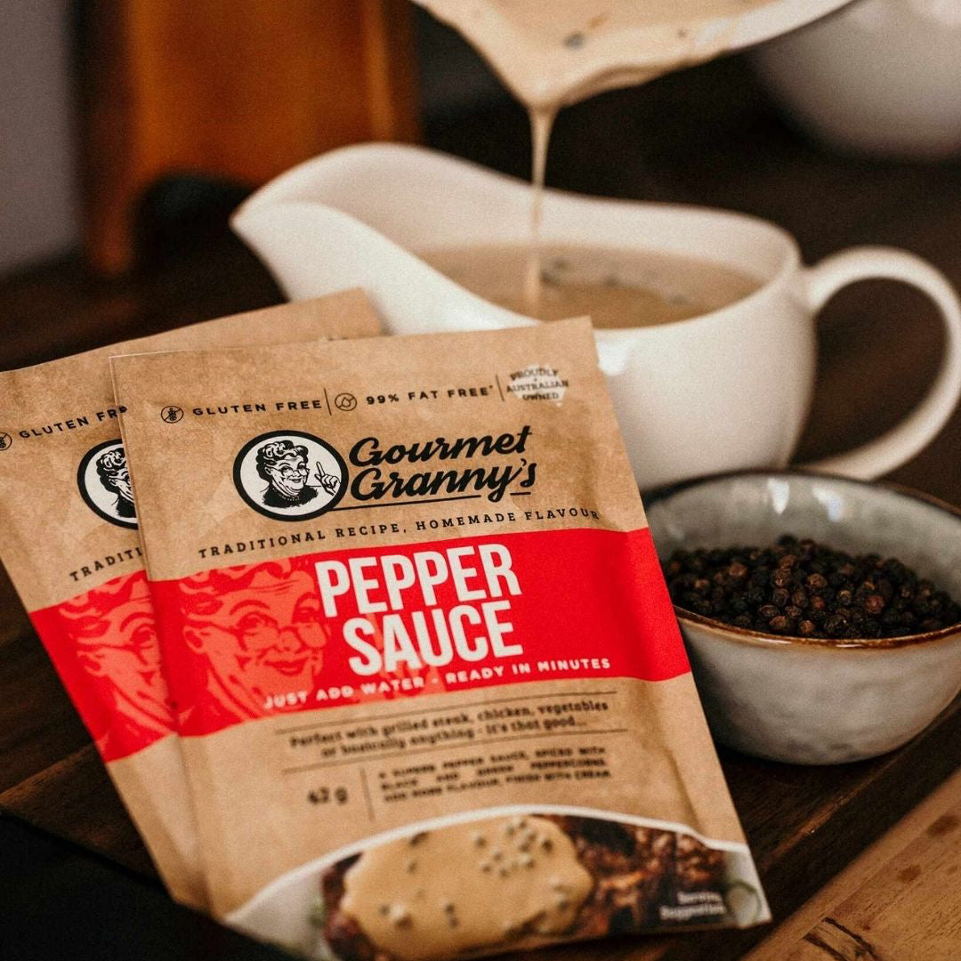 Gourmet Granny pepper sauce packets with a cup of pepper sauce and peppercorns in a bowl in the background.