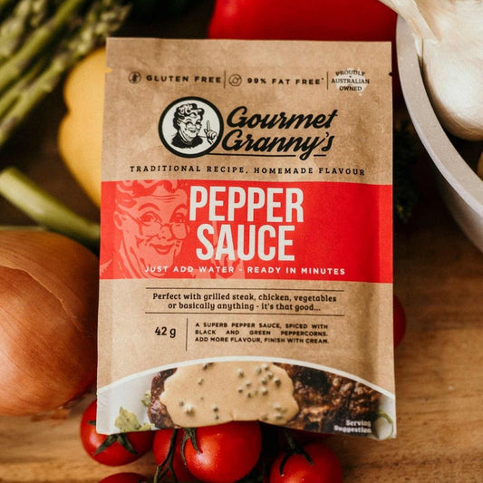 Gourmet Granny's Pepper Sauce packaging on a wooden surface with vegetables in the background